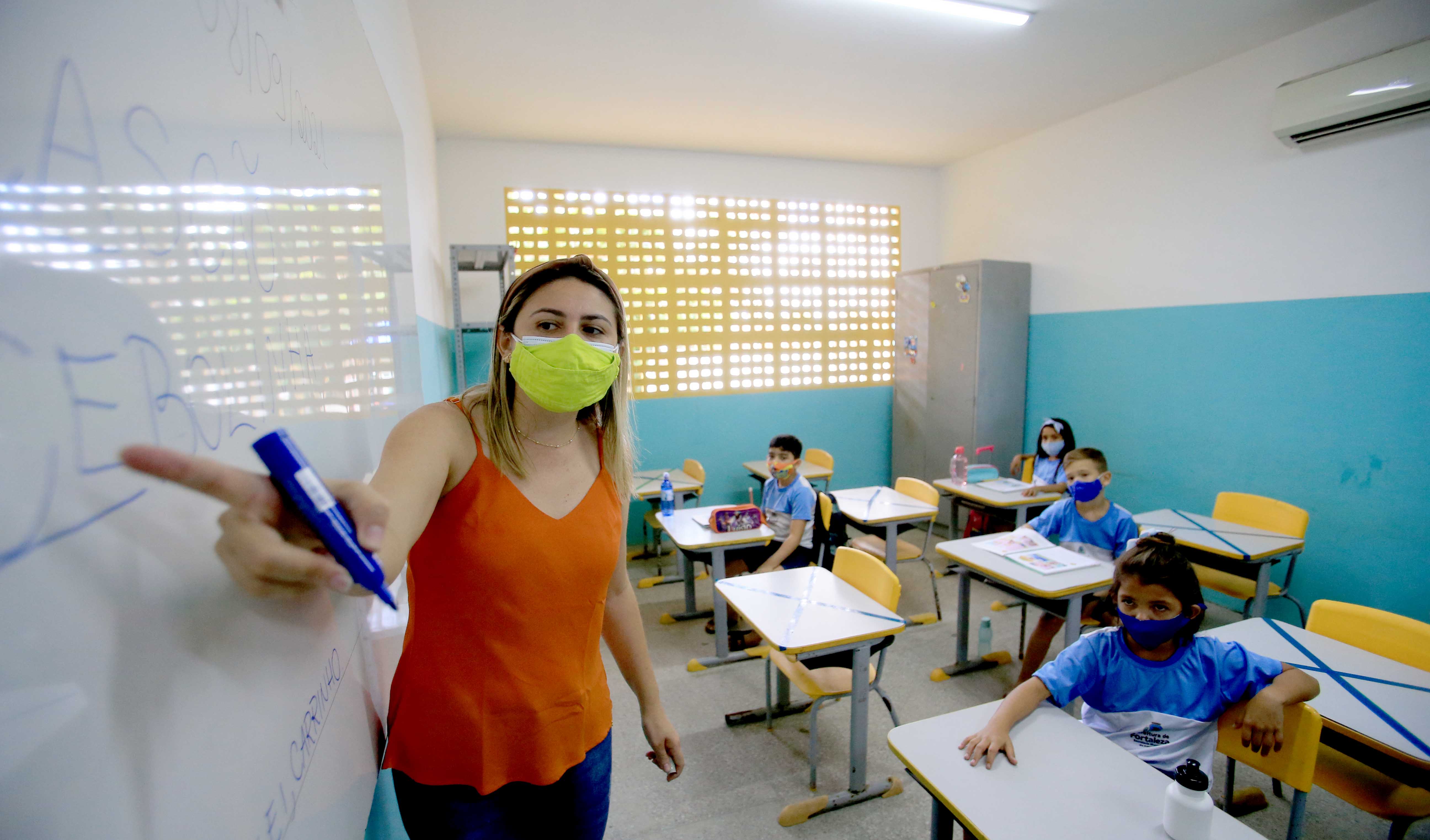 professora e alunos em sala de aula, todos usam máscara